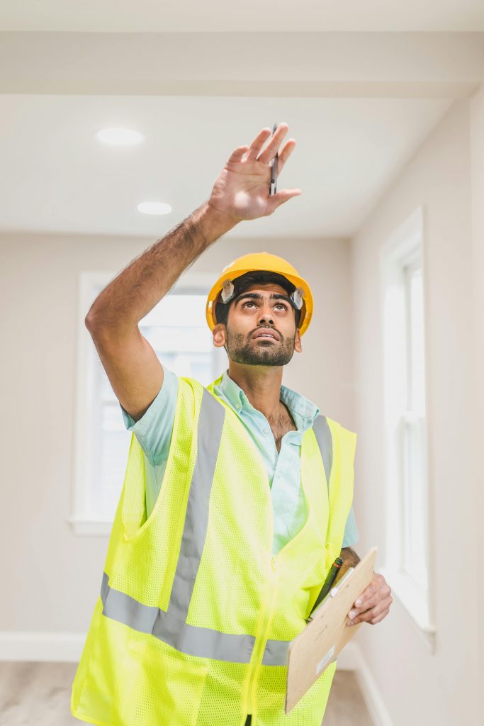 A construction worker inspecting a room while wearing a hardhat and safety vest indoors.